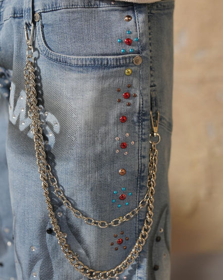 Close-up of blue jeans with decorative chains and beads.