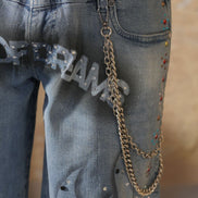 Close-up of blue jeans with embellishments and a chain, on a neutral background