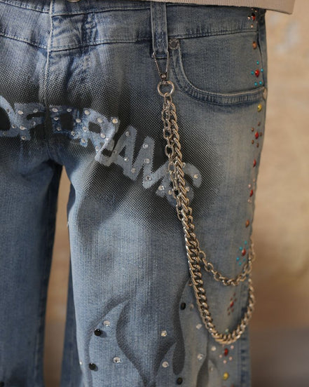 Close-up of blue jeans with embellishments and a chain, on a neutral background