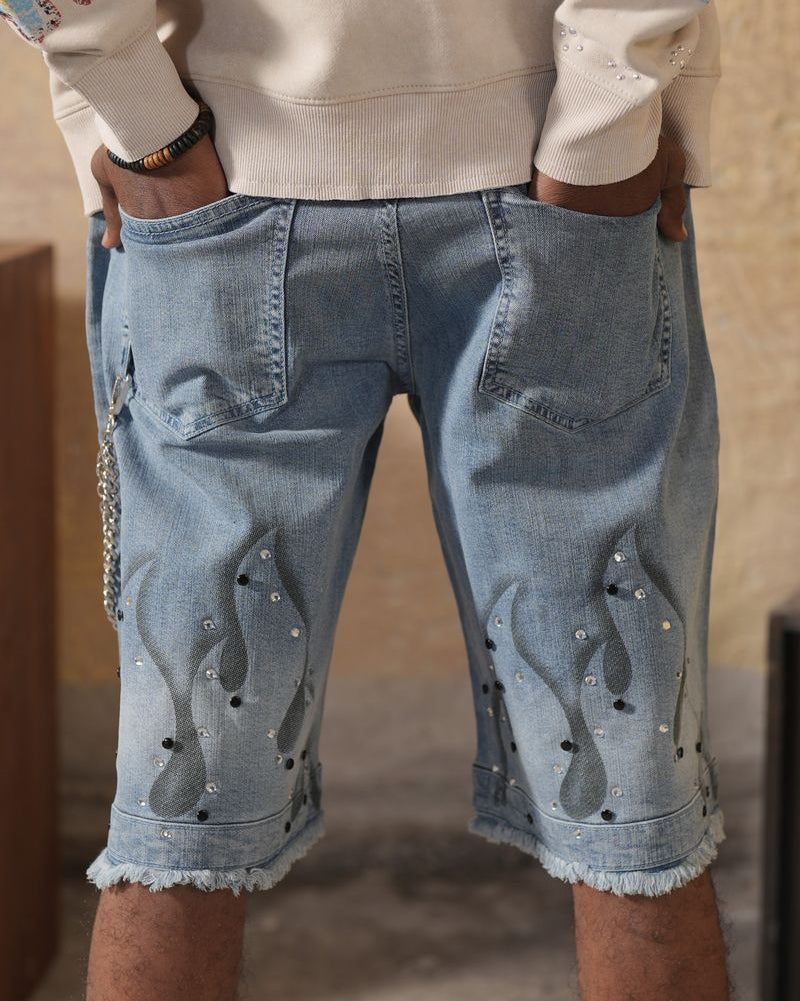 Person wearing light blue denim shorts with decorative elements, standing against a neutral background.