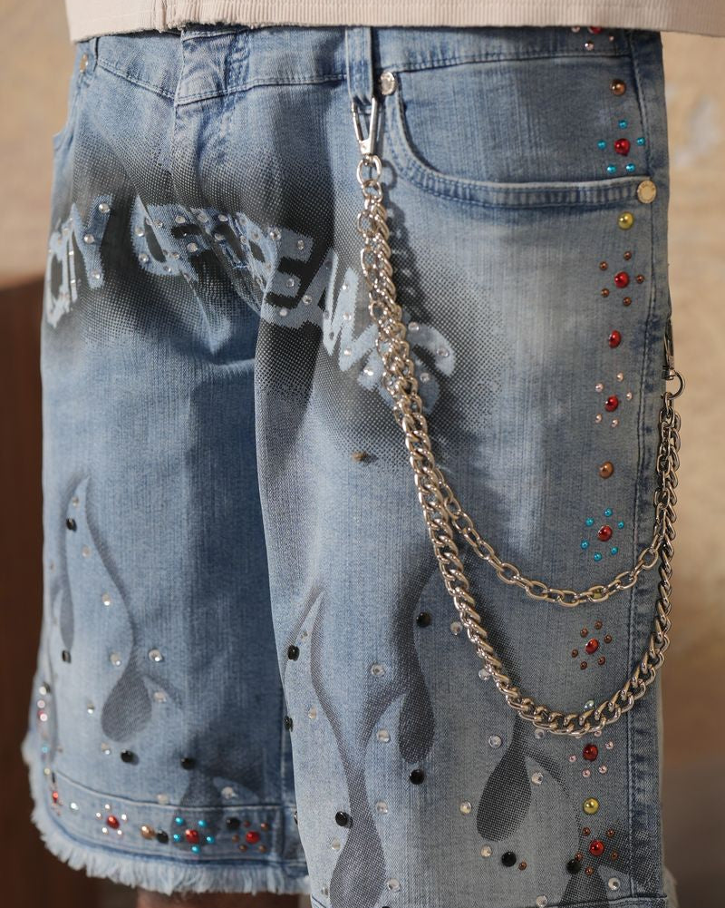 Denim shorts with embellishments and a chain detail on a plain background