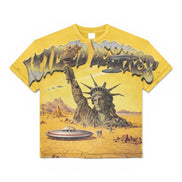A yellow graphic t-shirt featuring a surreal desert scene with the Statue of Liberty rising from the ground, flying ufo's, and large stylized text across the chest.