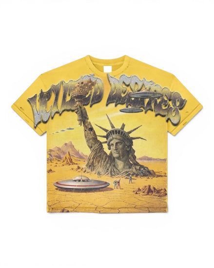 A yellow graphic t-shirt featuring a surreal desert scene with the Statue of Liberty rising from the ground, flying ufo's, and large stylized text across the chest.