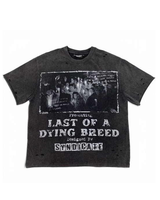A dark gray washed graphic t-shirt featuring a black-and-white band photo and distressed white text reading 'Presenting Last of a Dying Breed' and 'Designed by Syndicare'.