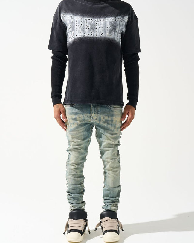 Person wearing a black long-sleeve shirt with white pattern and light blue jeans on a white background