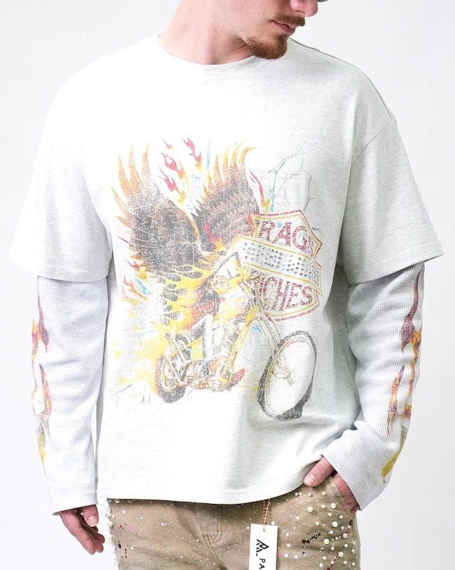 A man wearing a white long-sleeve t-shirt with a distressed graphic print of a motorcycle, flames, and wings, layered over a white long-sleeve base shirt. The photo is cropped from the chin down against a plain white background.