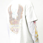 A man wearing a white long-sleeve graphic t-shirt, viewed from the back. The shirt features a large distressed eagle and shield graphic on the back with the text 'I RICHES' and 'JAZZ'.