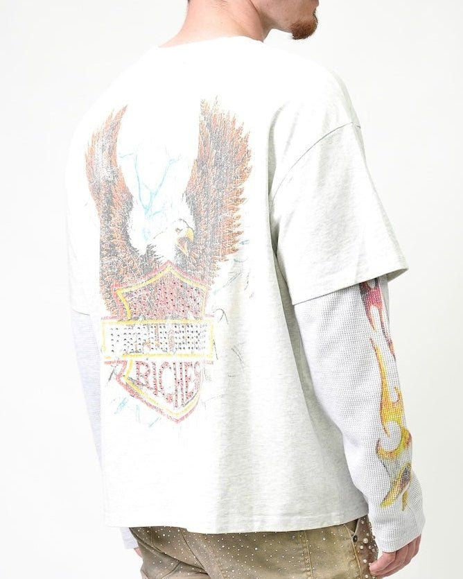 A man wearing a white long-sleeve graphic t-shirt, viewed from the back. The shirt features a large distressed eagle and shield graphic on the back with the text 'I RICHES' and 'JAZZ'.