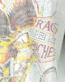 A close-up of a graphic t-shirt featuring a distressed, vintage-style illustration of a Native American figure with a feathered headdress and a bicycle, with the word 'RACE' printed in red on a white sign.