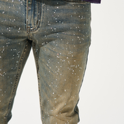 Close-up of a person wearing dark blue jeans with white speckles on a white background