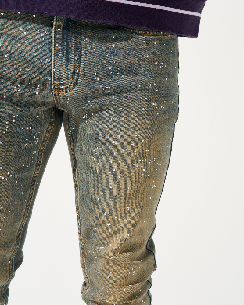 Close-up of a person wearing dark blue jeans with white speckles on a white background