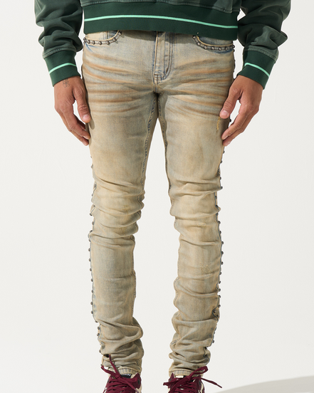 Person wearing beige distressed jeans with a green sweater and maroon sneakers on a white background