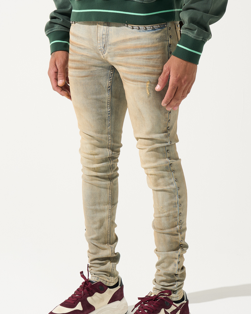 Person wearing beige distressed jeans and maroon and white sneakers on a white background