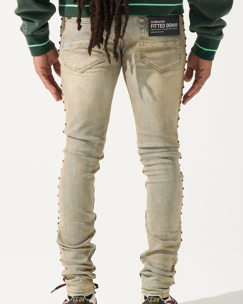 Person wearing beige jeans with decorative elements on a white background