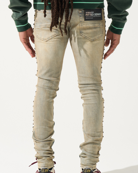 Person wearing beige jeans with decorative elements on a white background