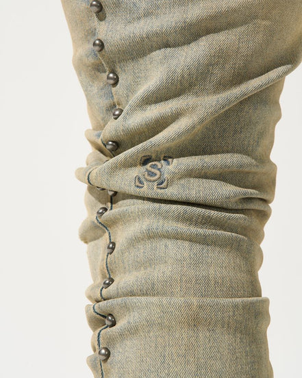 Close-up of beige denim pants with button details on a white background