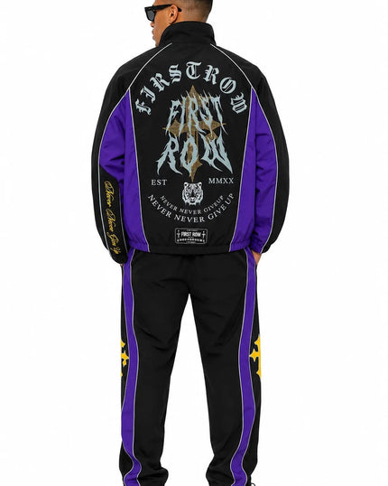 A man shown from the back wearing a black and purple track jacket and matching track pants with large graphic prints and white sneakers, photographed against a plain white background.