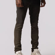 A model from the waist down wearing slim-fit dark brown jeans and chunky off-white sneakers, standing against a light gray studio background.