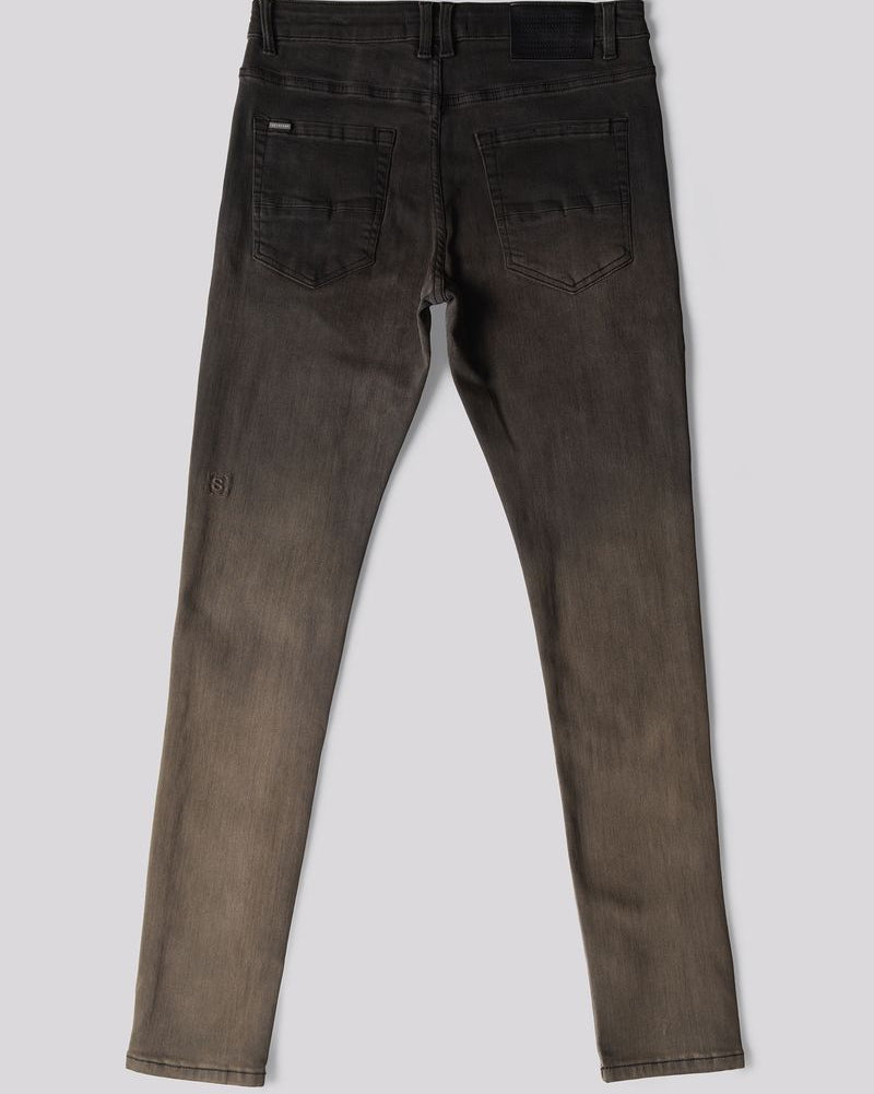 Back view of a pair of slim-fit jeans in a washed charcoal gray color, showing the back pockets and a subtle distressed detail on one leg, set against a solid gray background.