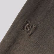 Close-up of a dark brown textured knit fabric with a tonal embroidered logo featuring an interlocking 'S' inside a square.