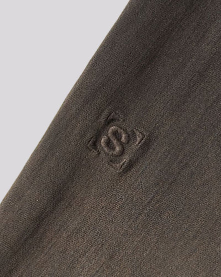 Close-up of a dark brown textured knit fabric with a tonal embroidered logo featuring an interlocking 'S' inside a square.