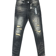 Distressed black denim jeans with ripped details showing beige lining, featuring a white vertical 'ANOM' logo on the right thigh, displayed flat against a white background.