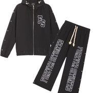 A two-piece black tracksuit set featuring a zip-up hooded jacket and matching sweatpants, both with white graphic text and decorative silver studs, displayed on a solid white background.