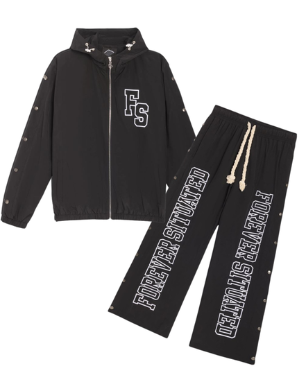 A two-piece black tracksuit set featuring a zip-up hooded jacket and matching sweatpants, both with white graphic text and decorative silver studs, displayed on a solid white background.