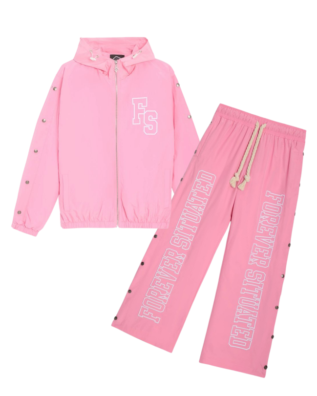 A pink two-piece tracksuit set featuring a zip-up hooded jacket and matching jogger pants. The jacket has a white outlined 'FS' logo on the left chest and silver-tone snap details along the sleeves and hem.