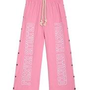 Pink wide-leg sweatpants with 'FOREVER SITUATED' printed vertically in white outline text on both legs, featuring a cream rope drawstring and black snap button details along the sides.