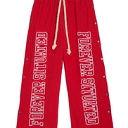 Red drawstring sweatpants with 'FOREVER SITUATED' printed vertically in white on both legs, accented with metal grommets along the sides.