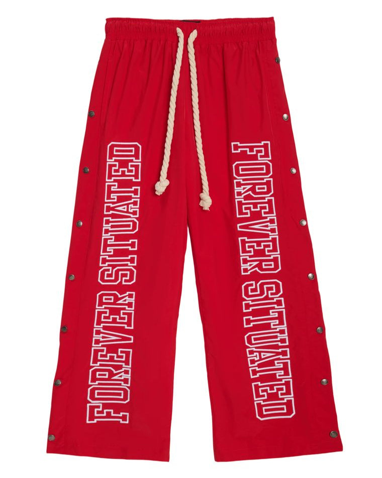 Red drawstring sweatpants with 'FOREVER SITUATED' printed vertically in white on both legs, accented with metal grommets along the sides.