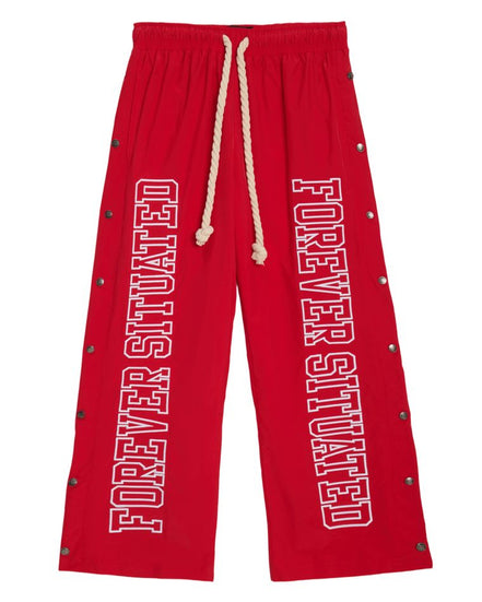 Red drawstring sweatpants with 'FOREVER SITUATED' printed vertically in white on both legs, accented with metal grommets along the sides.