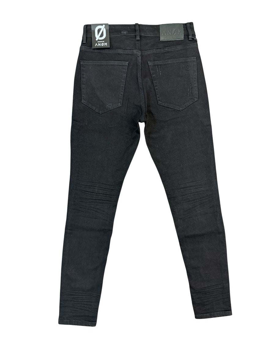 Black denim jeans shown from the back, featuring a dark wash with subtle whiskering and a visible ANOM brand patch on the back waistband.