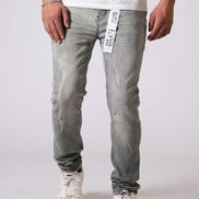 Person wearing light gray distressed jeans with a white label on a plain background