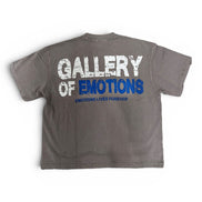 A gray short-sleeve t-shirt shown from the back, featuring a distressed graphic print that reads 'GALLERY OF EMOTIONS' in white and blue, with 'EMOTIONS LIVES FOREVER' printed below in blue.