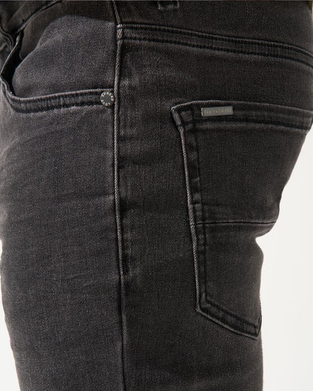 Close-up of black jeans with a visible brand label on a white background