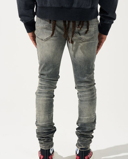 Person wearing gray distressed jeans and black shoes with red accents on a white background