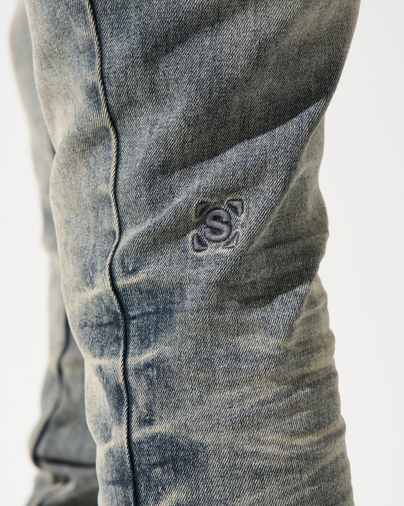 Close-up of a distressed denim jeans with a brand logo on a white background