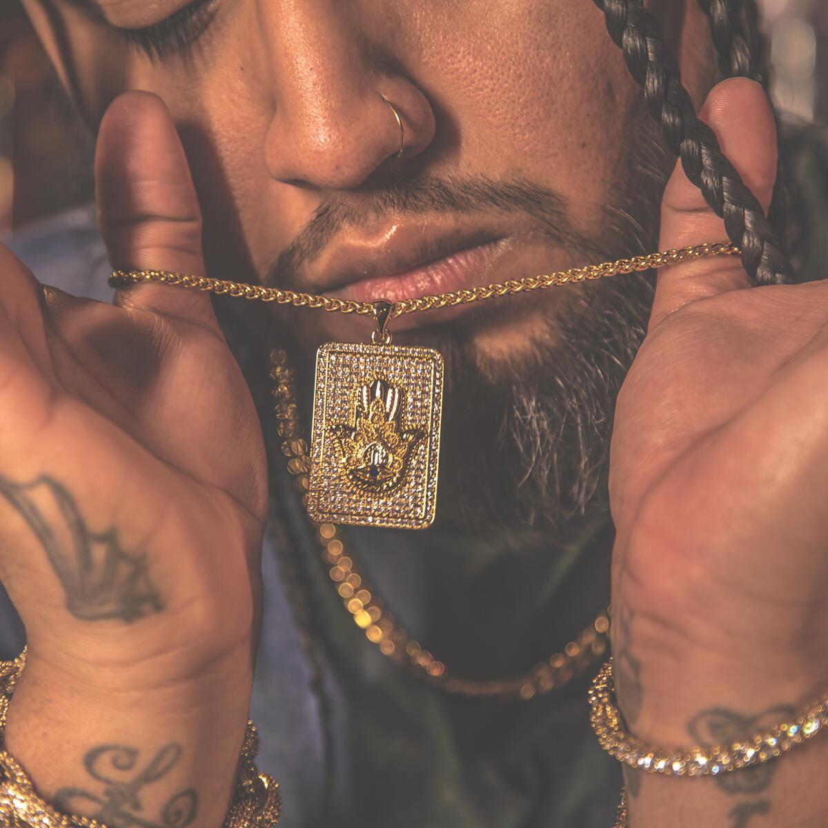 Man wearing a gold chain with a diamond-encrusted Hamsa hand pendant, close-up of face and hands.