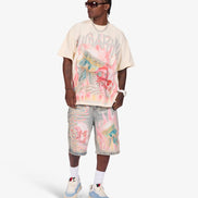 A model wearing a cream-colored Gucci t-shirt with a colorful graffiti-style graphic print, matching distressed denim shorts, white socks, and light blue and cream sneakers, set against a plain light gray studio background.