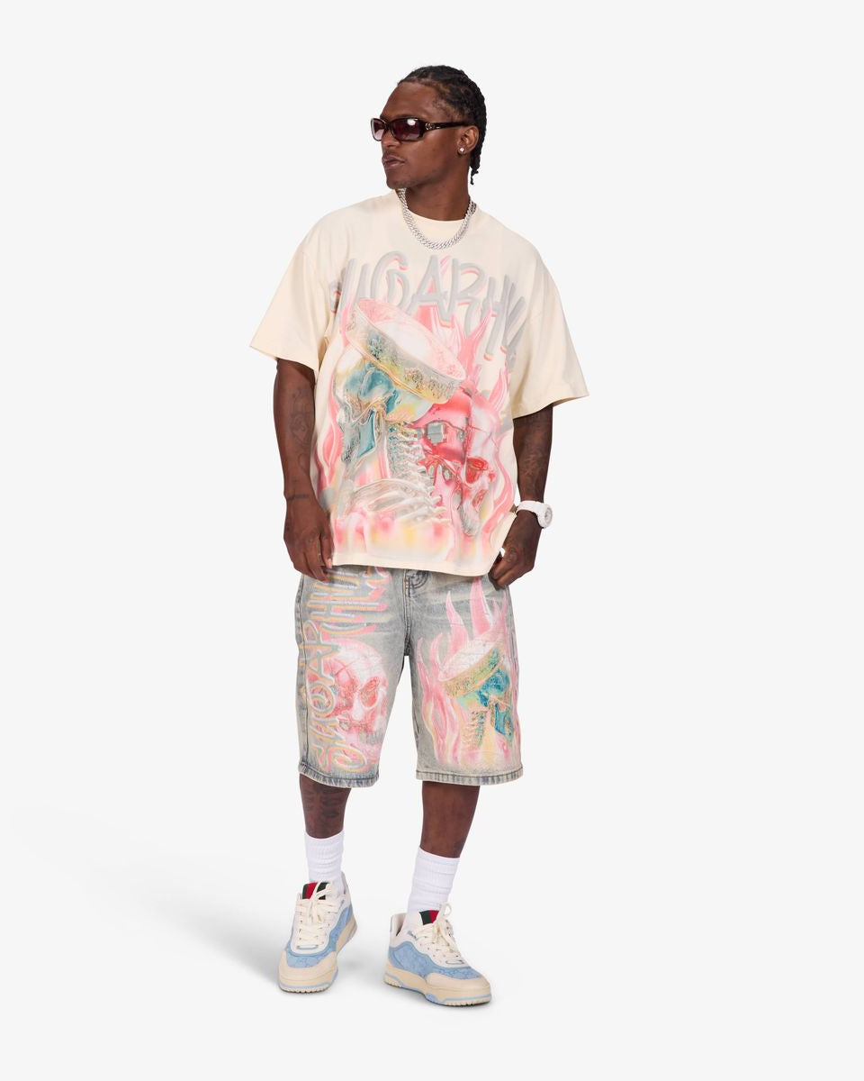 A model wearing a cream-colored Gucci t-shirt with a colorful graffiti-style graphic print, matching distressed denim shorts, white socks, and light blue and cream sneakers, set against a plain light gray studio background.