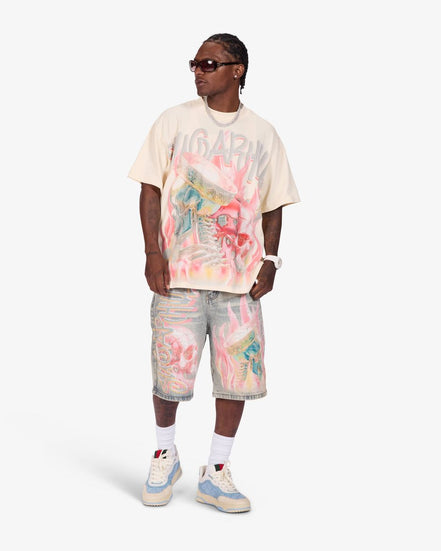 A model wearing a cream-colored Gucci t-shirt with a colorful graffiti-style graphic print, matching distressed denim shorts, white socks, and light blue and cream sneakers, set against a plain light gray studio background.