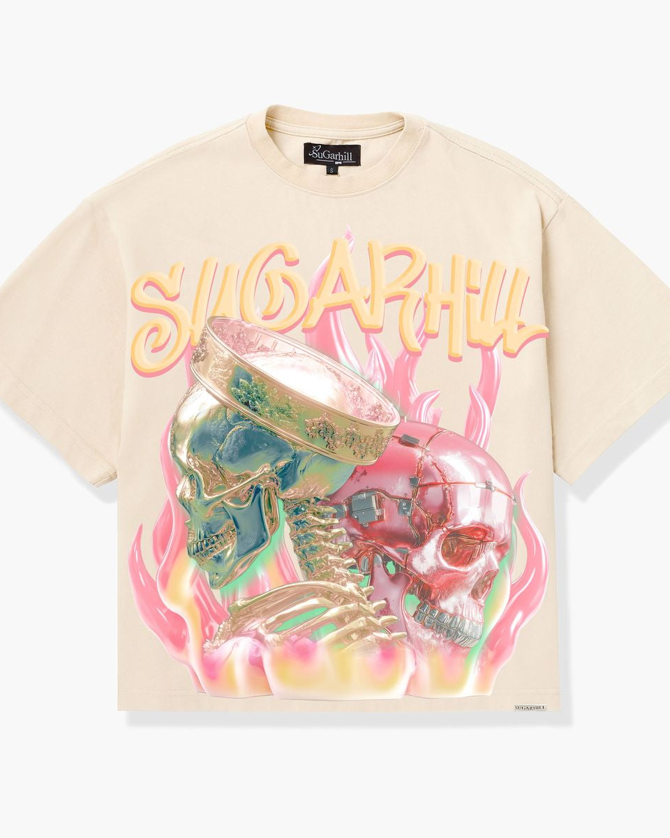 A cream-colored short-sleeve graphic t-shirt featuring a large front print of two skulls in green and pink with flames and the text 'SUGARHUL'.