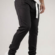 Person wearing black jogger pants with a visible brand logo on a light gray background
