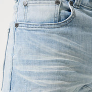 Close-up of light blue denim jeans with stitching details on a white background