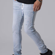 A person wearing light-wash distressed skinny jeans with a black t-shirt and black platform sneakers, shown from the waist down against a solid gray studio background.