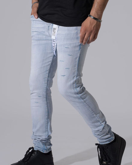 A person wearing light-wash distressed skinny jeans with a black t-shirt and black platform sneakers, shown from the waist down against a solid gray studio background.