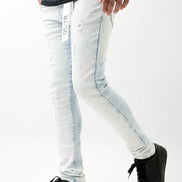 Person wearing light blue jeans with a brand logo and black sneakers on a white background