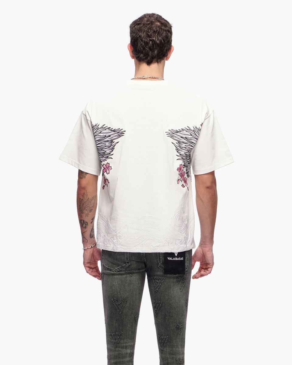 Person wearing a white t-shirt with black and red designs on the back, standing against a white background.
